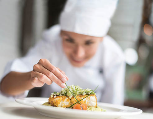Cook decorating a plate and putting the ultimate touches - focus on foreground 